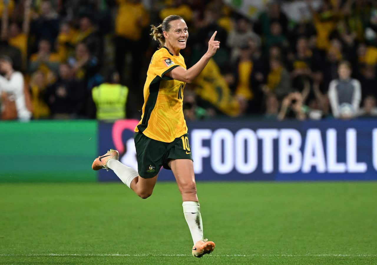 A woman in a yellow football shirt raises her right index finger