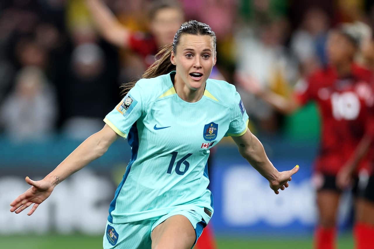 A woman in a teal football shrt with arms outstretched.